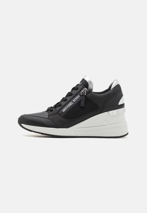Czarno-białe sneakersy na koturnie z fakturowaną czarną cholewką, bocznym zamkiem błyskawicznym, logo Michael Kors i grubą białą podeszwą na jednolitym tle.