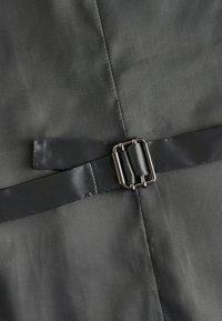 Tissu gris foncé avec des lignes de couture visibles et une ceinture en satin noire avec une boucle rectangulaire argentée au milieu.