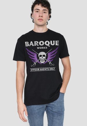 Young man wearing black t-shirt with purple winged skull, crossed swords, and text "BAROQUE WORKS OFFICER AGENTS ONLY," blue jeans.