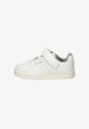 Zapatilla de cuero blanca con interior gris, que presenta una correa de velcro y lados perforados. Diseño sencillo con suela de goma y tacón plano.