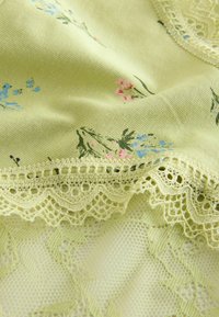 Lichtgroene stof met een bloemmotief van roze en blauwe bloemen. Omrand met delicate kantafwerking, wat textuur en detail toevoegt.