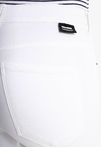 Jeans de ganga branca com um bolso traseiro e uma etiqueta de marca preta visível. As características incluem detalhes de costura e uma textura suave.