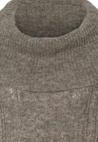 Gros plan d'un pull gris tricoté avec un col roulé côtelé épais et un motif torsadé sur le corps.