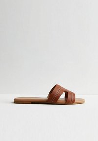 Sandalo scorrevole in pelle marrone con due larghe cinghie, finitura testurizzata e sottili accenti di cucitura. Design piatto e minimalista con una suola liscia.