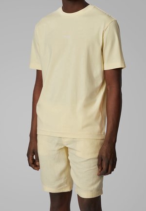 Jasnożółta bawełniana koszulka z krótkim rękawem i dekoltem okrągłym, z małym białym logo "BOSS" na piersi, zestawiona z dopasowanymi szortami.