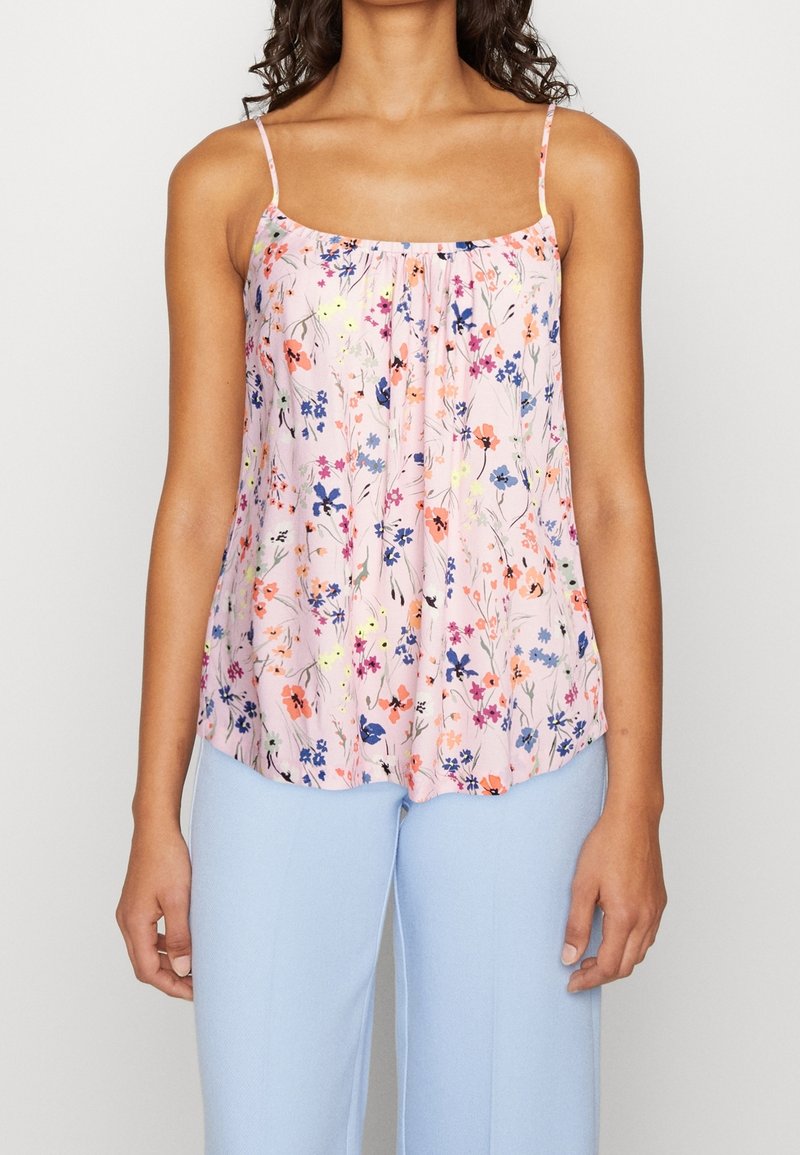 Femme portant un haut sans manches rose avec un imprimé floral multicolore et un pantalon bleu clair, montrée du cou aux hanches.