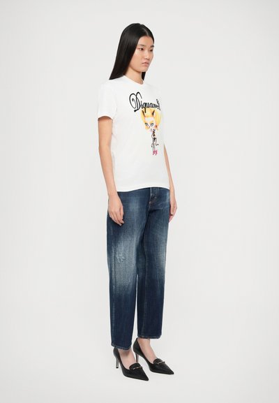 T-shirt grafico bianco con un personaggio illustrato colorato, abbinato a jeans blu scuro scoloriti e tacchi neri a punta.