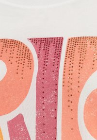 Camiseta blanca con un diseño de texto grande en degradado de colores rosa y naranja, adornada con pequeños strass brillantes para añadir textura.
