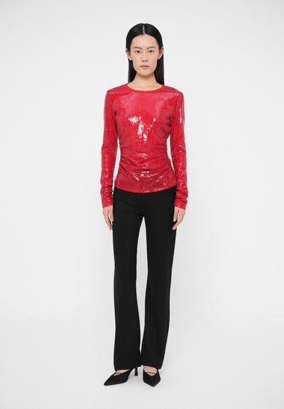 Punaste litritega pika varrukaga topp ümarate kaelustega, millele on lisatud mustad kohandatud püksid ja mustad terava ninaga kontsakingad. Sile tekstuur, kehaleistuv disain.