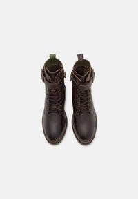 Bottines en cuir marron avec des orteils ronds, un laçage sur le devant et des sangles à boucle. Fini texturé et détails de doublure intérieure contrastants.