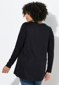 Sort langærmet top med rund halsudskæring, let buet kant og blød tekstur; båret med blå jeans.