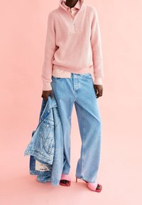 Pull rose côtelé, chemise rose clair en dessous, jean large bleu clair, tenant une veste en denim et portant des sandales à talons roses.