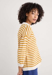 Pull rayé jaune et blanc, avec un col rond, des manches trois-quarts et un ourlet côtelé. Texture tricot douce.