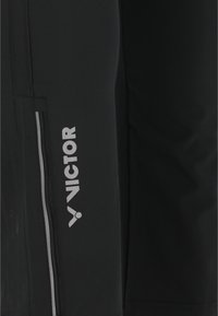 Svarta sportshorts med en slät yta, försedda med en silverfärgad dragkedjeficka och en framträdande vit logotyp på sidan.