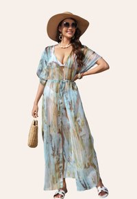 Vêtement de plage transparent avec une taille nouée, présentant un motif abstrait bleu et marron, des manches kimono et un design fluide. Porté avec un chapeau de soleil.