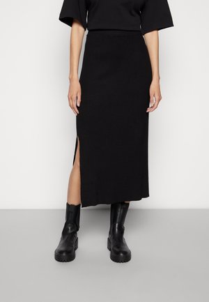 Zwarte, knielange geribbelde rok met een schuine split aan de zijkant, gecombineerd met robuuste zwarte enkellaarzen. De stof heeft een gladde textuur en een rekbare pasvorm.