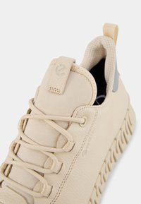 Sneaker in pelle beige con tomaia testurizzata, lacci elasticizzati e suola in gomma beige. Presenta una linguetta e dettagli con logo GORE-TEX.