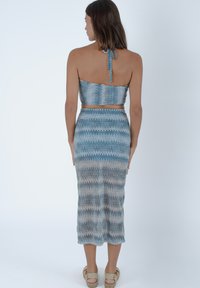 Set di due pezzi blu e beige con una top halter corta e una gonna di lunghezza media decorata con disegni a zigzag e una silhouette aderente.