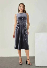 Grå fløyels midi-kjole med et tettsittende liv, ärmeløs design og rynkedetaljer i midjen, som faller under kneet.