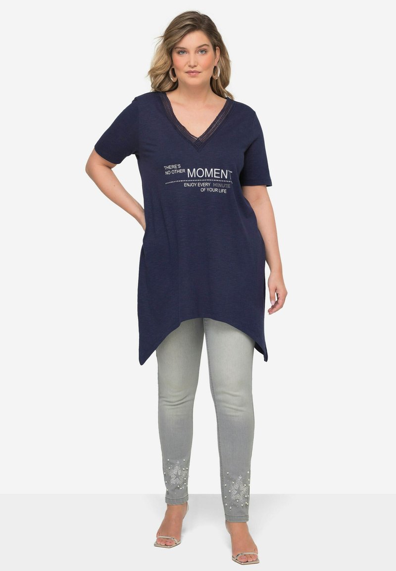 Túnica navy con escote en V y mangas cortas, con texto en blanco. Combinada con jeans ajustados de color gris claro adornados con patrones de estrellas.