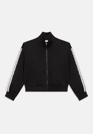 Juoda užtraukiama striukė su aukštu apykakle ir baltomis banguotomis juostelėmis abiejose rankovėse, elastingais rankogaliais ir liemeniu.