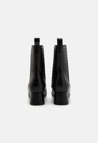 Botines de cuero negro con un acabado suave, tacón bajo en bloque, con remaches metálicos a los lados y tiradores en la parte trasera.