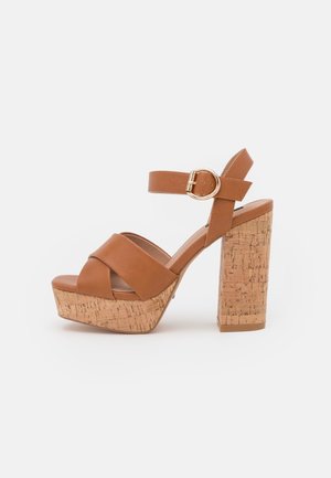 Brown faux leather platform sandals with cork block heel, crisscross straps, adjustable ankle strap, and gold-tone buckle detail.