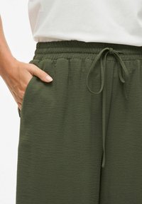 Olivově zelené, lehké kalhoty s elastickým pasem, šňůrkou na stáhnutí a bočními kapsami; texturovaná látka se zdá být mírně pomačkaná.