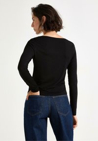 Svart långärmad skjorta med bred halsringning, kombinerad med högmidjade blå jeans med kontrasterande sömmar och två bakfickor.