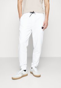Witte joggingbroek met zijzakken, elastische boorden en een tailleband met trekkoorden. Voorzien van een klein rood en zwart logo-opdruk op de heup.