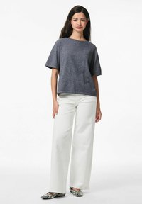 Top grigio a maniche corte con scollatura rotonda, abbinato a pantaloni bianchi a gamba larga e ballerine a righe bianche e nere su uno sfondo semplice.