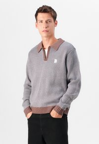 Gray knit sweater with a brown polo collar and ribbed cuffs. Features a half-zip front and small logo on the left chest.