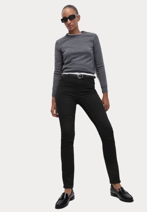 Svarta jeans i kombination med en grå långärmad tröja, med en vit undertröja, kompletterat med svarta loafers och rektangulära solglasögon.