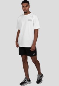 Bílý bavlněný tričko s krátkým rukávem a potiskem na hrudi. Spárováno s černými šortkami s bílým nápisem, doplněno sportovními botami.