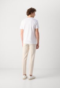 Hvit kortermet t-skjorte kombinert med lyse beige skreddersydde bukser og hvite joggesko. Enkelt design uten synlige mønstre eller logoer.