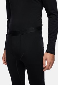 Black thermal leggings with a smooth texture, featuring a wide waistband marked 'VAUDE,' and contrasting stitching details.