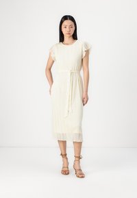 Robe en dentelle de couleur blanc cassé avec des manches courtes à volants, une taille ceinturée et un ourlet mi-long, ornée de motifs floraux en bas.