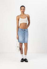 Denim krilo ima visok pas, sprednje zapiranje na gumbe in ozek kroj v zbledeli modri barvi; kombinirano z bež kratkim topom in črnimi loaferji.