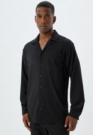 Camisa negra de manga larga con cuello de muesca, bolsillo frontal y cierre de botones; tela suave con una textura sutil.