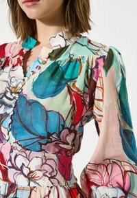 Bunt bedruckte Bluse mit leichtem, transparentem Stoff. Sie hat einen Rüschensaum, eine geknöpfte Vorderseite und lange Puffärmel.