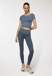 Niebieski zestaw odzieży sportowej składający się z krótkiego topu z rękawami i legginsów z wysokim stanem, wykonany z gładkiego, elastycznego materiału.