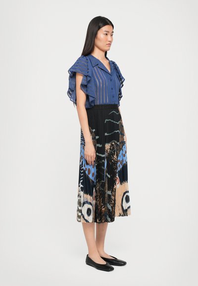 Blue striped blouse with ruffled sleeves, paired with a colorful patterned pleated skirt featuring abstract designs. Black flat shoes complete the look.