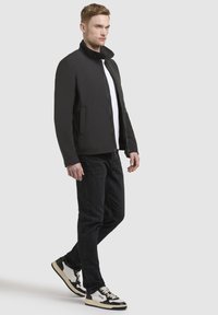 Black, structured jacket with a high collar and zip closure, paired with a white shirt and black jeans, accentuated by sporty sneakers.