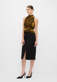 Blusa senza maniche con scollo a halter in stampa floreale, abbinata a una gonna a tubino nera con una fessura frontale. Indossata con tacchi a punta neri.