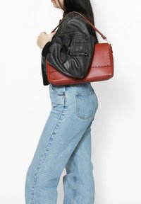 Rode handtas met een gestructureerd ontwerp, gedragen over de schouder. Voorzien van soepel leer en decoratieve stiksels.
