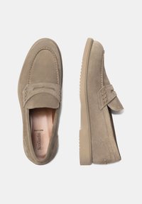 Mocassins en daim beige avec un bout arrondi, des détails cousus et une lanière surélevée sur le dessus. Semelle en caoutchouc pour une meilleure adhérence.