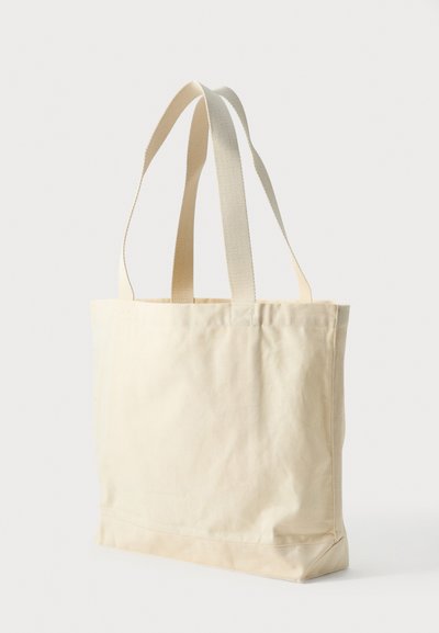 Μπεζ υφασμάτινη τσάντα tote με δύο μακριές λαβές, όρθια σε φωτεινό φόντο.