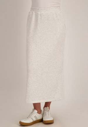 Vrouw die een hooggesneden, lichtgrijze, enkellange rok draagt gecombineerd met witte sneakers met rubberen zolen.