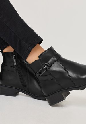 Bottines en cuir noir avec fermeture éclair latérale, ornées d'une boucle décorative et de détails de couture. Talon bas, texture lisse et épurée.