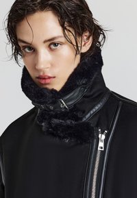Schwarze Jacke mit einem strukturierten Kunstpelzkragen, Lederakzenten und Reißverschlussdetails. Verfügt über ein hohes Kragen-Design und eine schlanke, taillierte Silhouette.